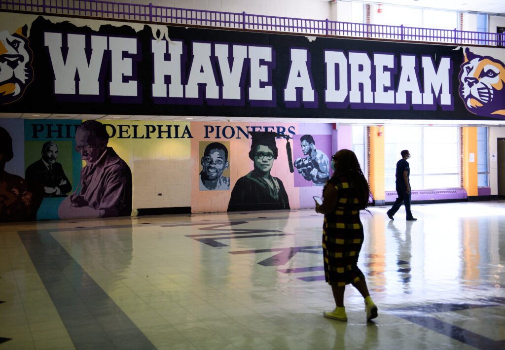 A school official walks in front of a sign in a cavernous hall that reads “We Have a Dream.”